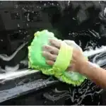 Pessoa lavando carro com esponja verde.