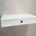 Prateleira branca com gaveta na parede.